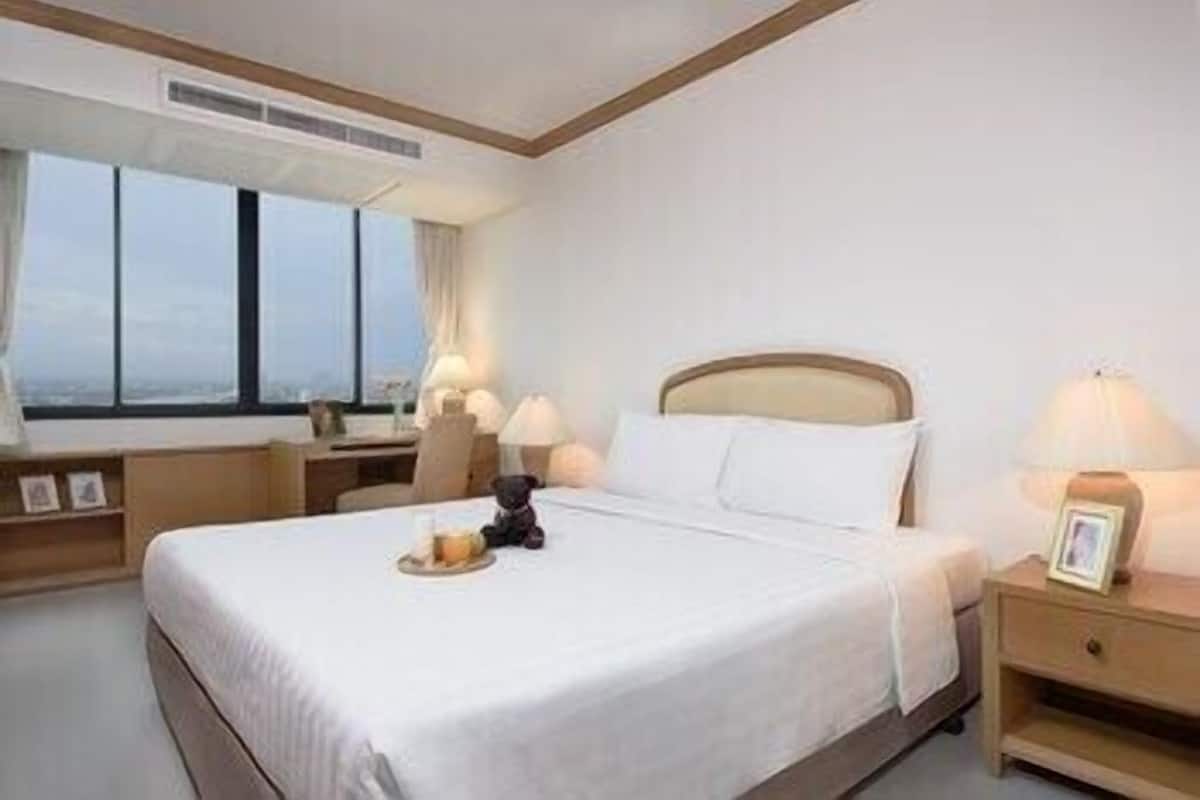 Une chambre d’hôtel avec un grand lit, des lampes de chevet, une table de chevet, un bureau et une fenêtre avec des rideaux.