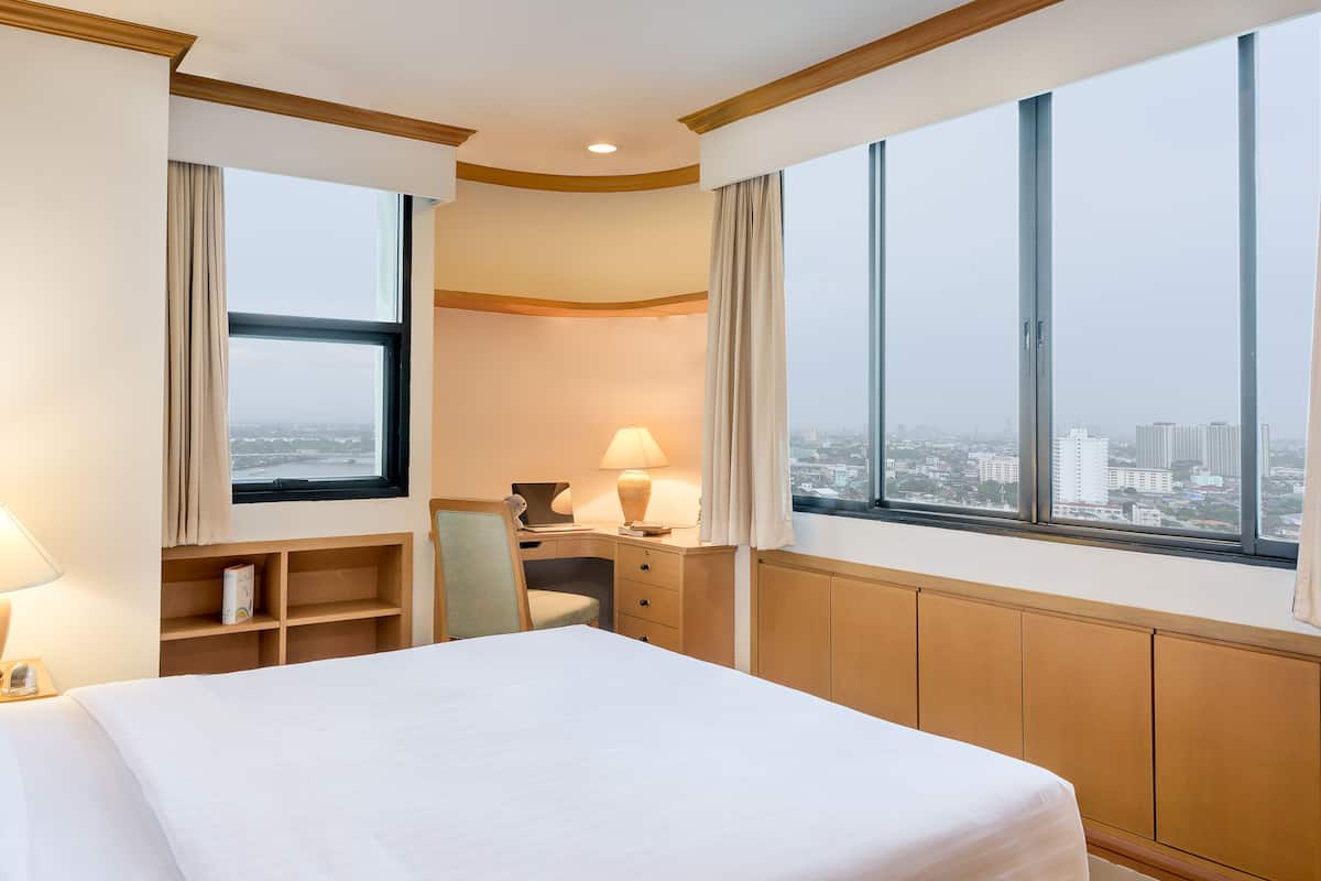Une chambre d’hôtel avec un grand lit, un bureau, une chaise et une vue sur la ville grâce à de grandes fenêtres.