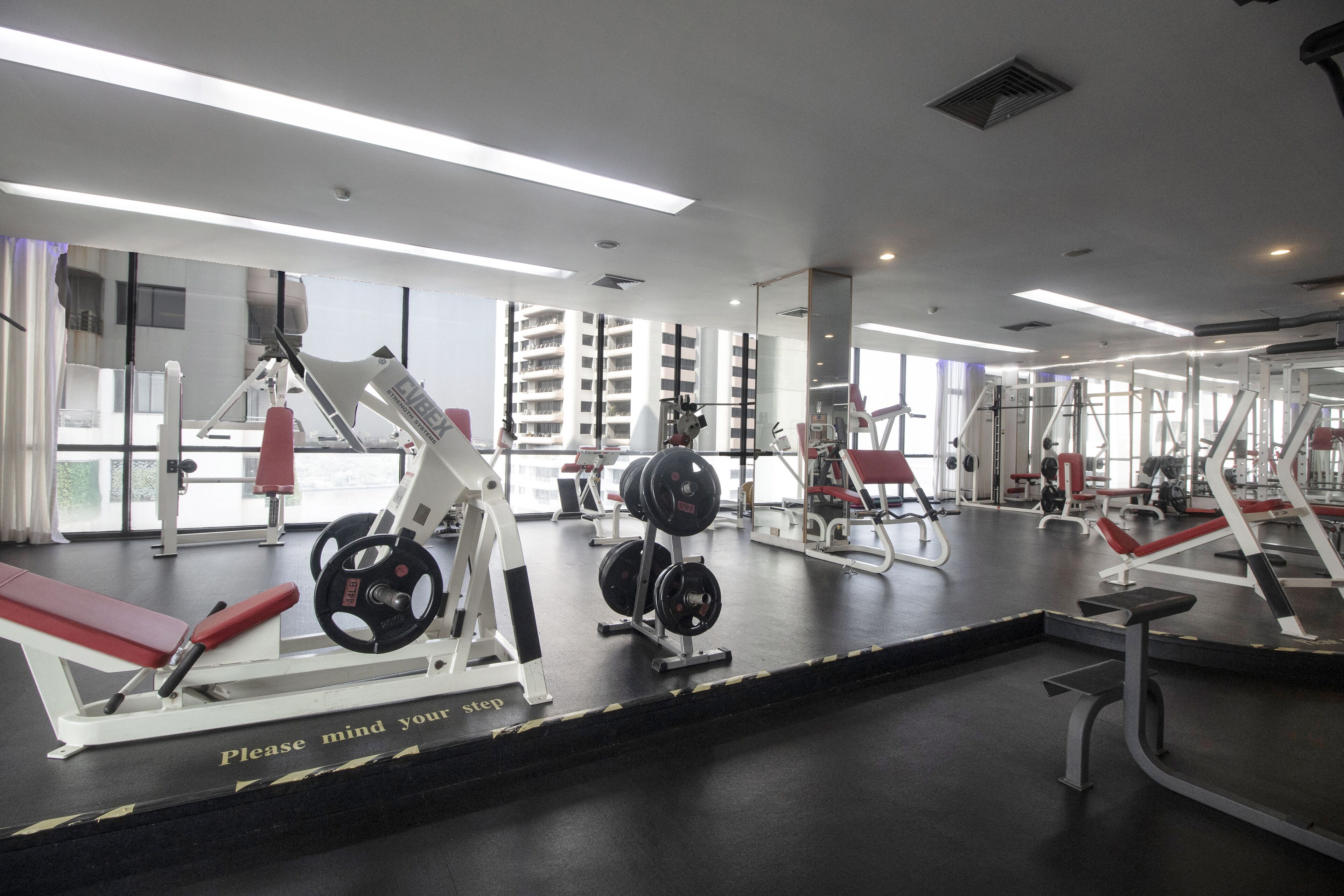 A gym with various exercise equipment, large windows, and a caution sign on the floor.