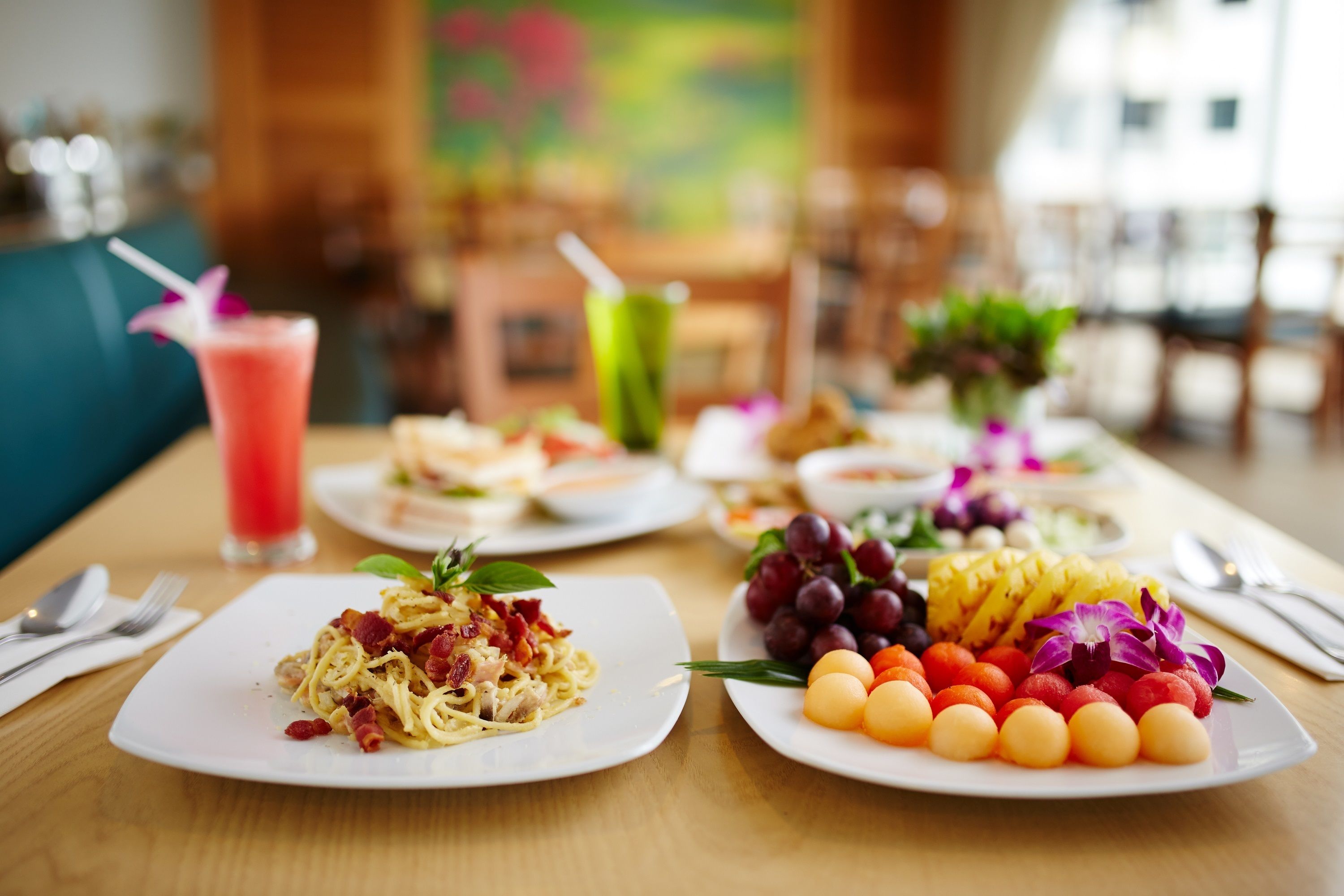 Une table à manger avec des assiettes remplies de nourriture, notamment des pâtes, des fruits et une boisson.