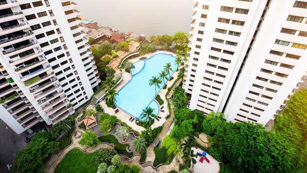 Un edificio alto con piscina rodeado de vegetación y palmeras.