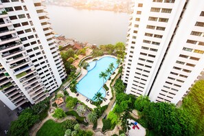 A high-rise building with a swimming pool surrounded by greenery and palm trees.
