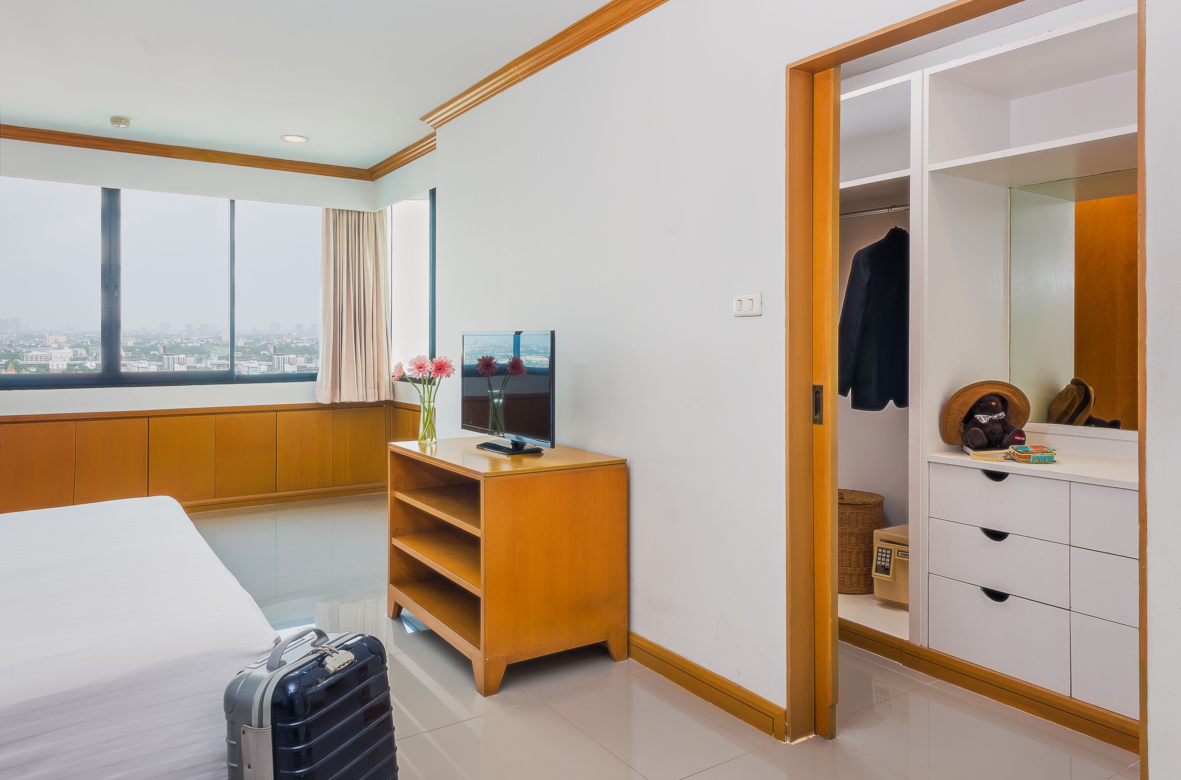 Une chambre d’hôtel avec un lit, une commode en bois, une télévision et une grande fenêtre donnant sur la ville.