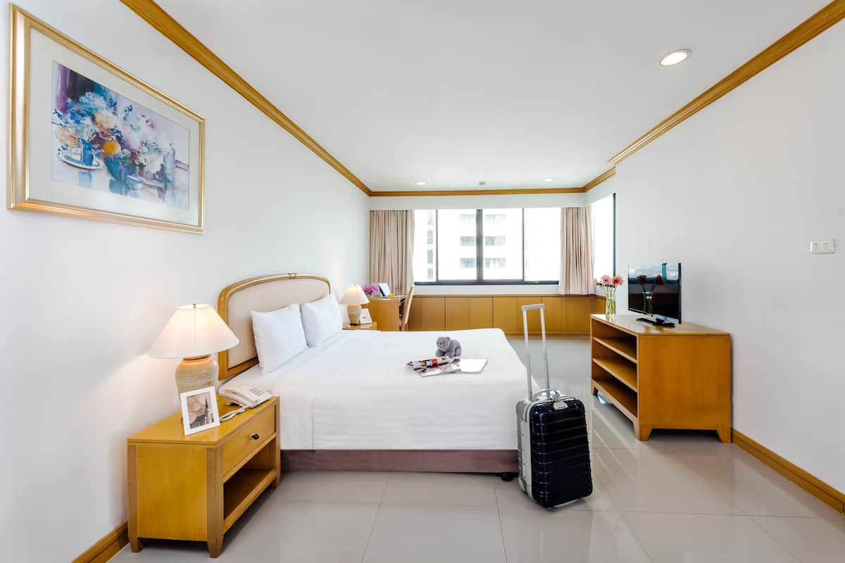 Une chambre d’hôtel avec un lit, une table de chevet, une lampe, un cadre photo, un meuble pour la télévision et une valise.