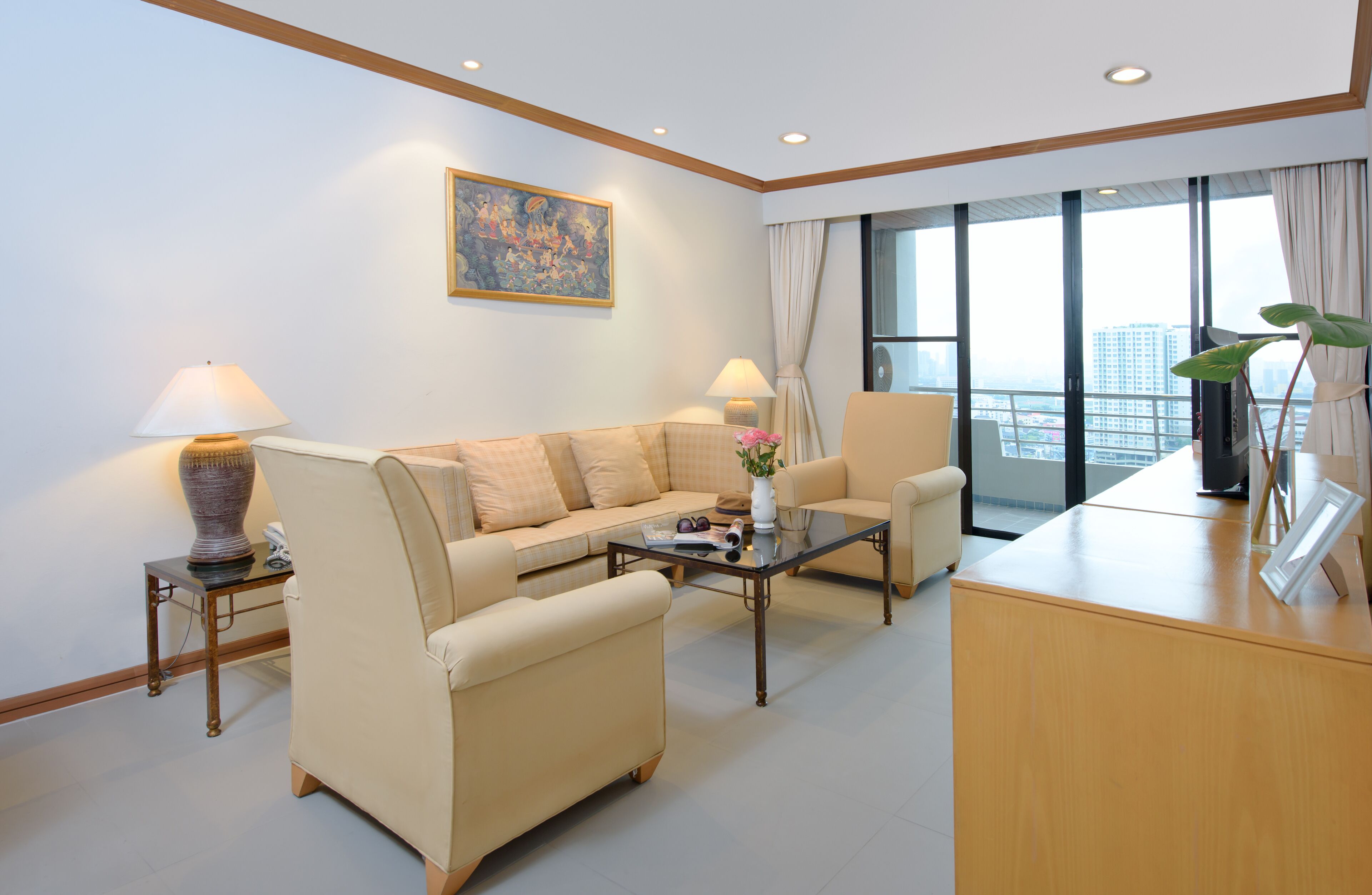 Une chambre d’hôtel moderne, équipée d’un canapé, d’un fauteuil et d’un bureau. Un tableau orne le mur, une fenêtre est agrémentée de rideaux et offre une vue sur la ville.