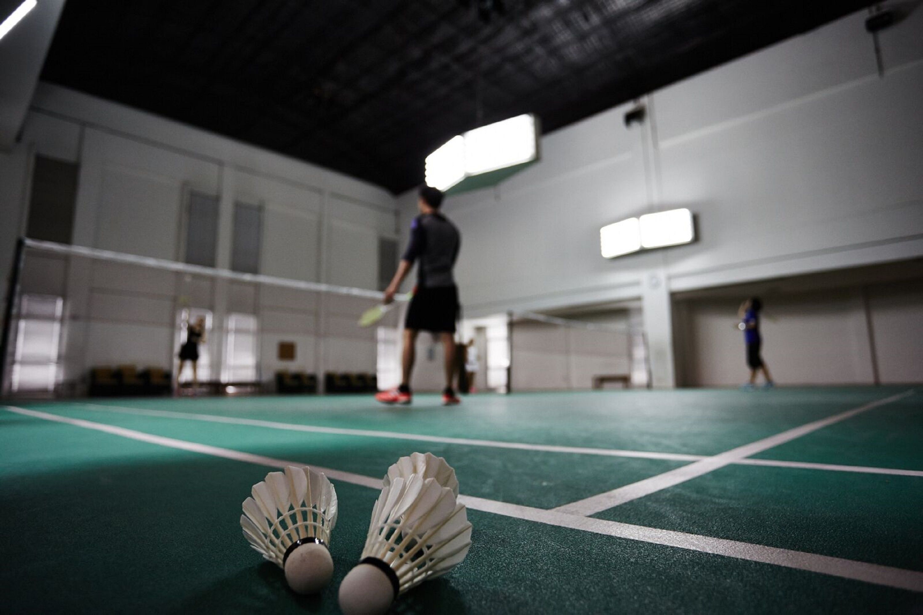 Ein Badmintonfeld mit Hähnenbällen im Vordergrund und Spielern im Hintergrund.