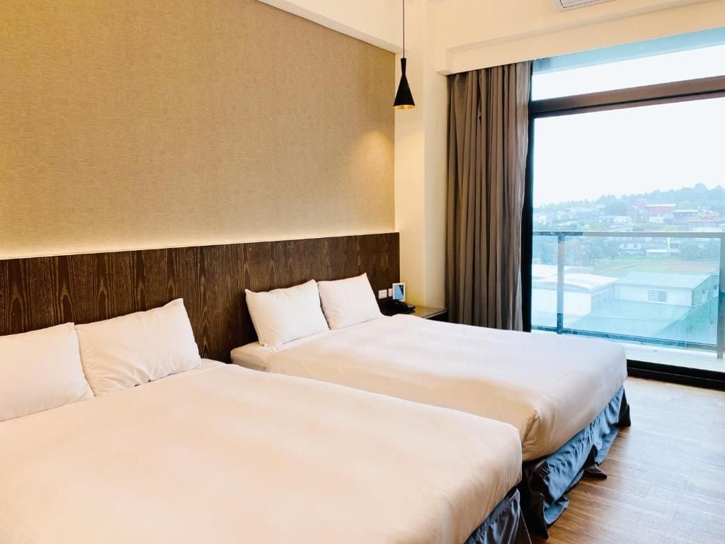 A hotel room with two beds, a large window with a view, and a modern design.