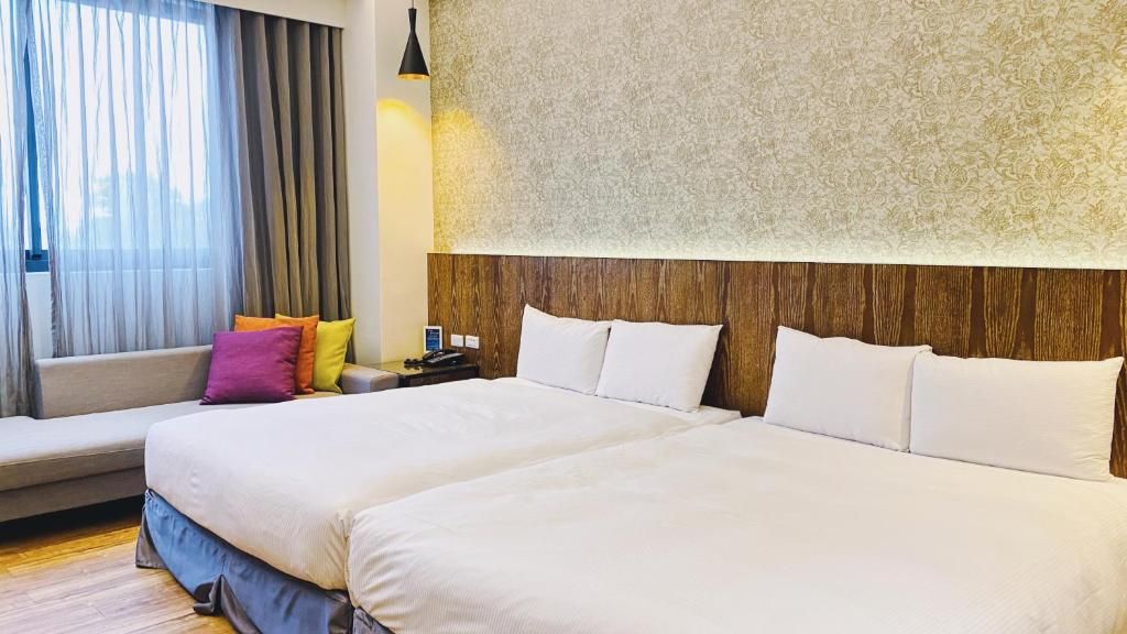 Habitación de hotel con dos camas, un sofá, una mesita de noche y una ventana con cortinas.