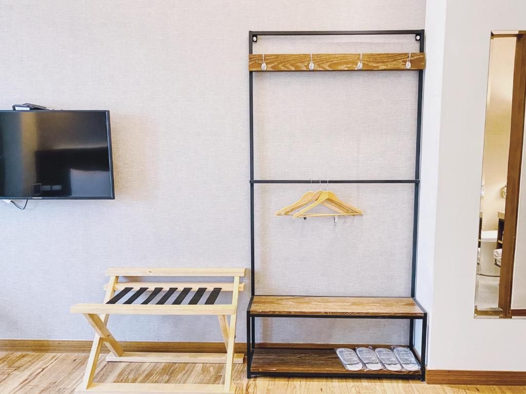 Een kamer met een wandtelevisie, een houten bankje, een wandplank met kledinghangers en een schoenenrek.