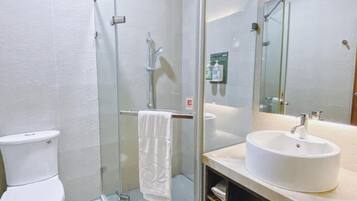 Un baño con ducha envuelta en vidrio, un lavabo blanco y un inodoro.
