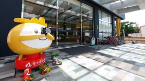 L’entrée d’un immeuble, avec une grande mascotte, une porte en verre et un espace réservé au stationnement des vélos.