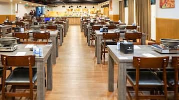 A restaurant with multiple tables and chairs, a counter with a display of food, and a kitchen area in the background.