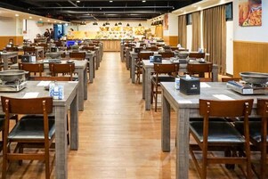 Un restaurante con varias mesas y sillas, una barra con una exhibición de comida y una zona de cocina al fondo.