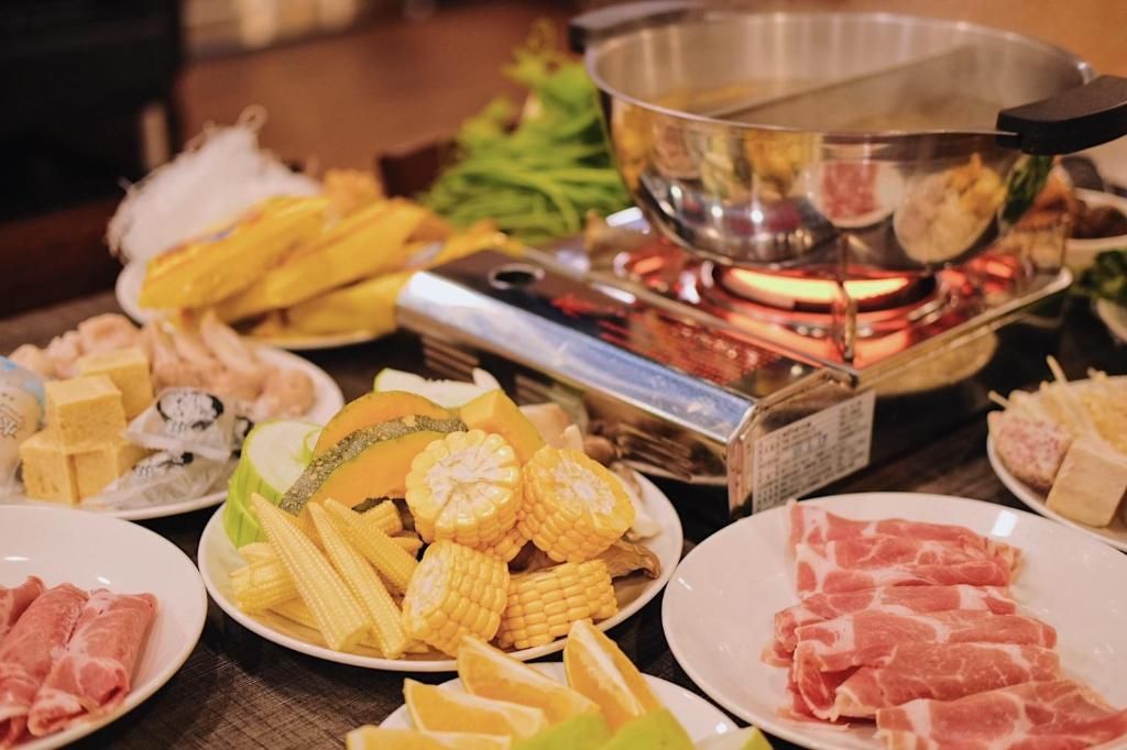 A variety of food items including corn, meat, and vegetables arranged on a table with a hot plate.