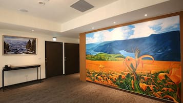A hotel lobby with a large painting of a landscape, a reception desk, and a door.