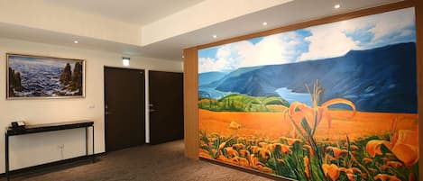 Un hall d’hôtel avec un grand tableau représentant un paysage, un comptoir d’accueil et une porte.