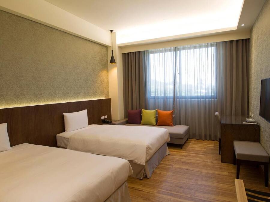 A hotel room with two beds, a desk, a chair, a TV, and a window with curtains.