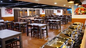 Une cafétéria spacieuse, dotée de nombreuses tables et chaises, un buffet proposant différents plats et une grande fresque murale.
