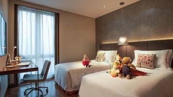 Een hotelkamer met twee bedden, een bureau en een stoel. Op de bedden liggen decoratieve kussens en knuffeldieren.