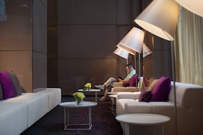A modern hotel lobby with a sofa, armchairs, and a coffee table. There are lamps and a vase with flowers on the table. - Modena by Fraser Zhuankou Wuhan (Wuhan)