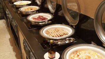 A buffet line with various food items, including sausages, eggs, and meats, arranged on a counter with lids.