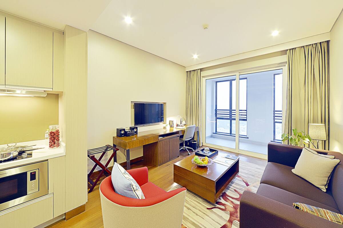 Un salon moderne avec un canapé, une table basse, un téléviseur et un balcon agrémenté de rideaux.