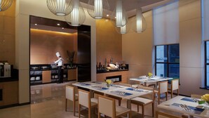 A modern dining area with tables set for service, a chef preparing food, and contemporary lighting fixtures. - Modena by Fraser Zhuankou Wuhan (Wuhan)