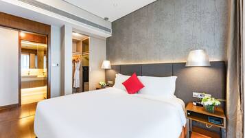 A hotel room with a large bed, bedside lamps, a nightstand with a vase of flowers, and a wardrobe with a mirror.