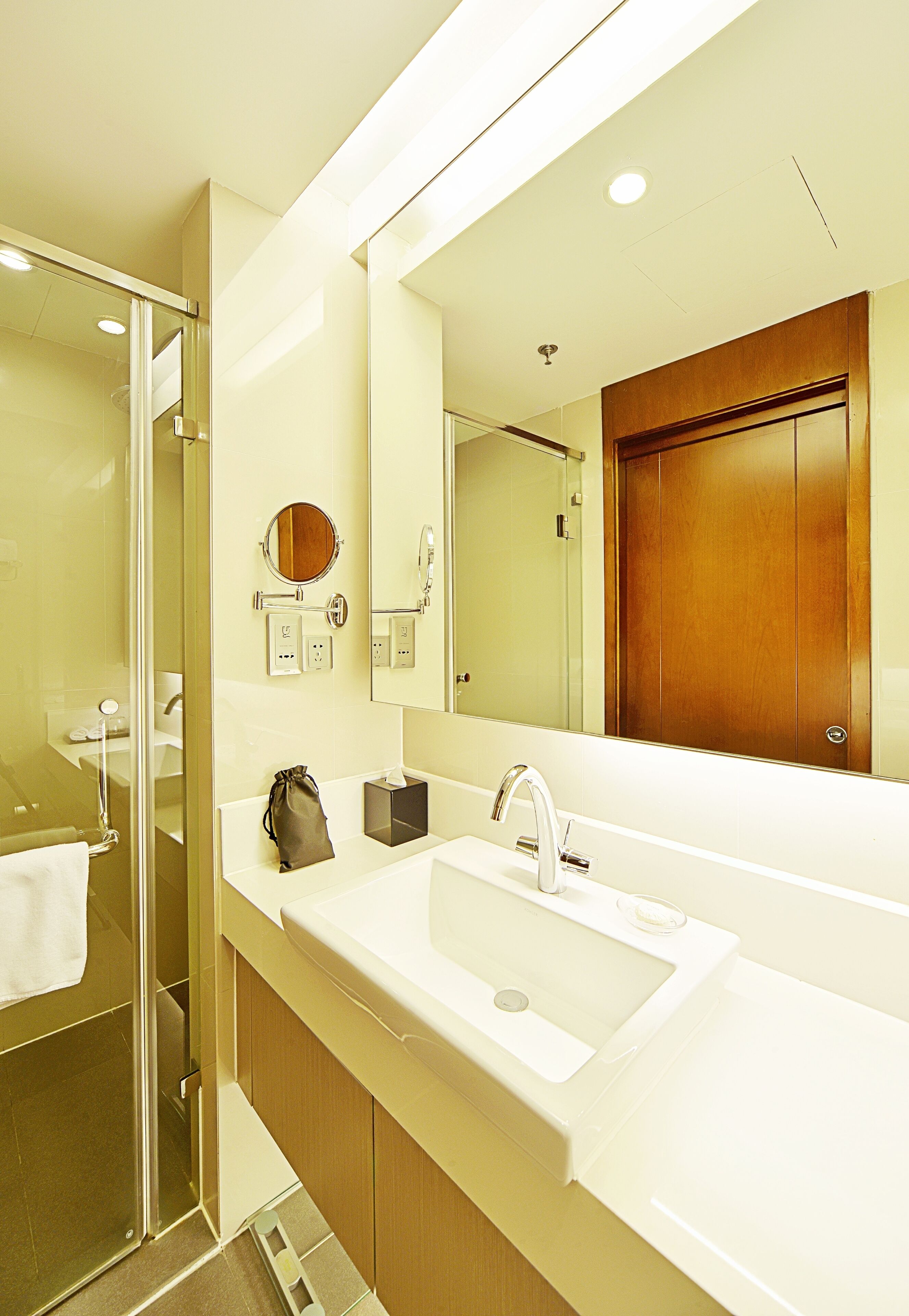 A modern bathroom with a glass shower enclosure, a large mirror, and a wooden door.