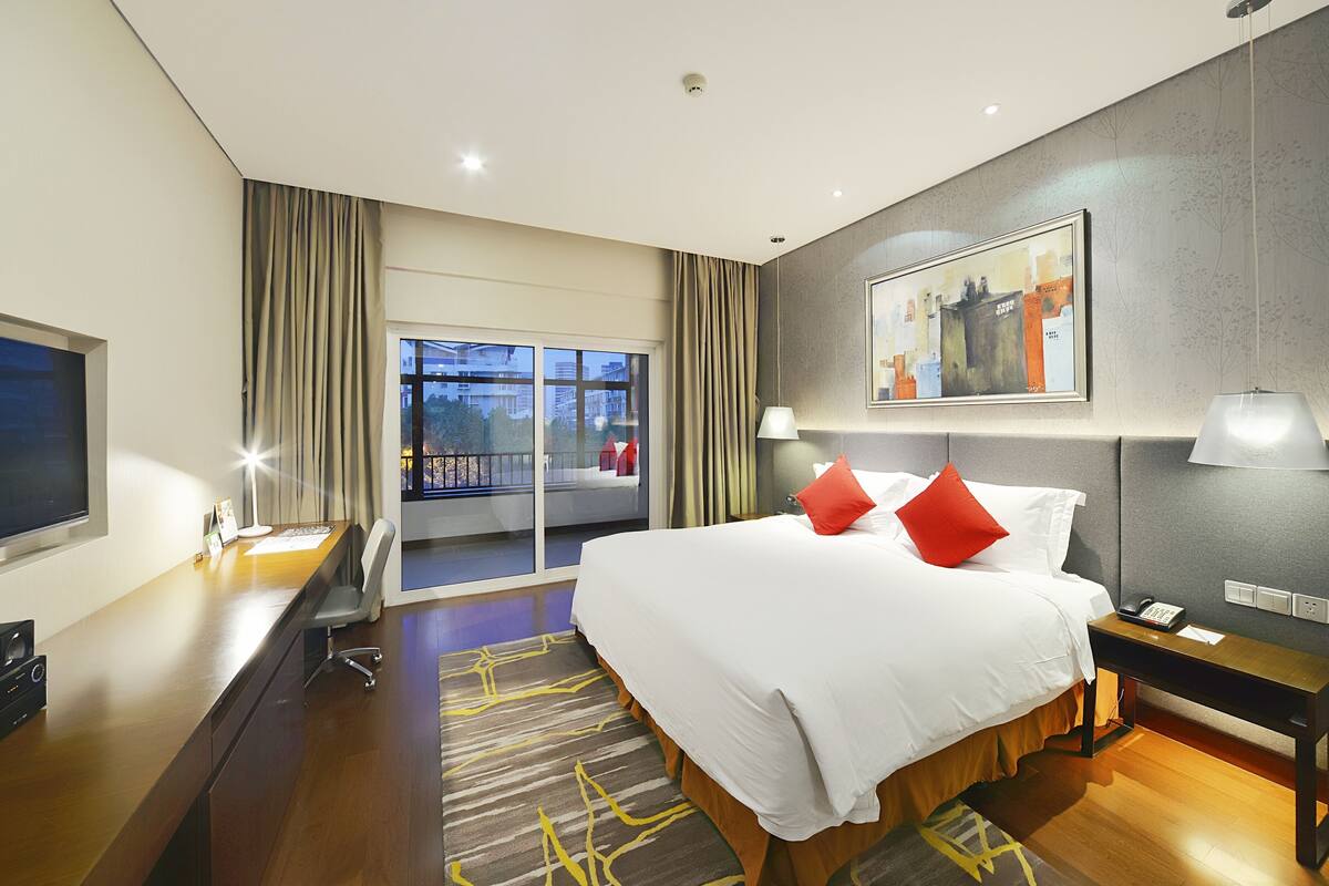 Une chambre d’hôtel avec un grand lit, un bureau avec un ordinateur, une télévision et un balcon donnant sur les bâtiments.