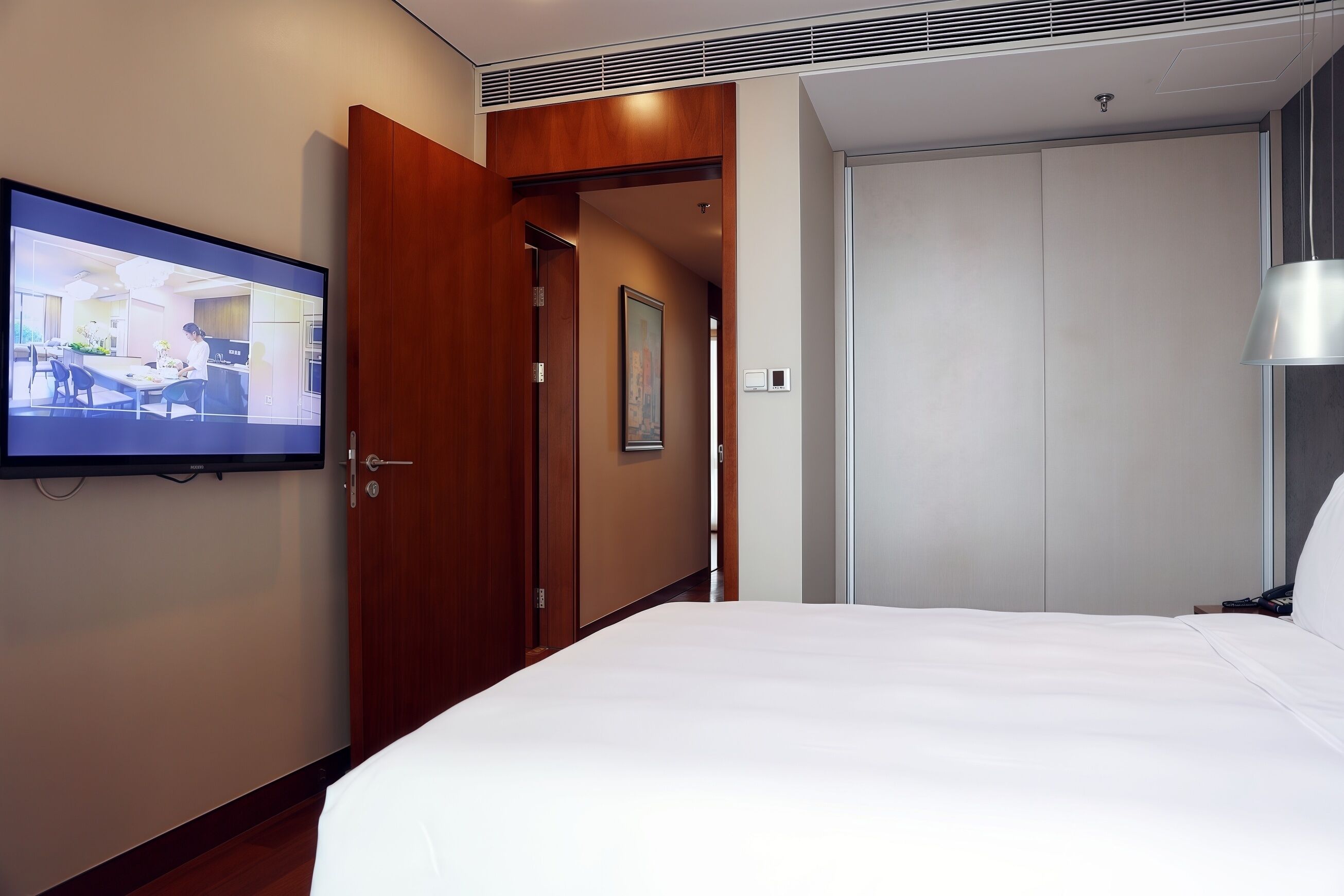 A hotel room with a bed, a television mounted on the wall, a wooden door, and a closet.