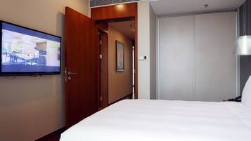 A hotel room with a bed, a television mounted on the wall, a wooden door, and a closet.