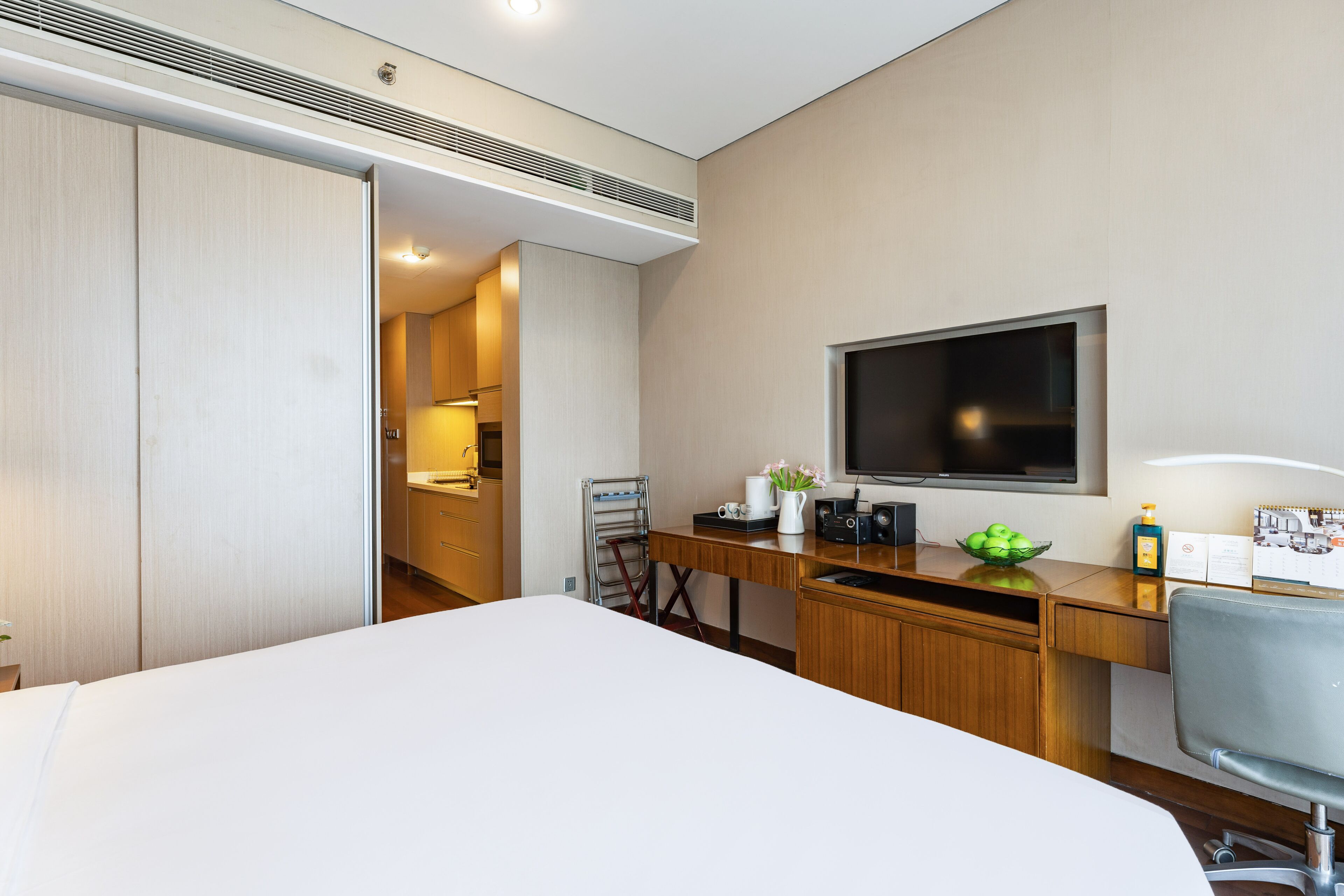A hotel room with a bed, a desk with a computer, a television, and a bathroom visible through an open door.