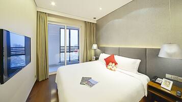 A hotel room with a bed, a TV, a bedside table with a lamp, a phone, and a picture frame.