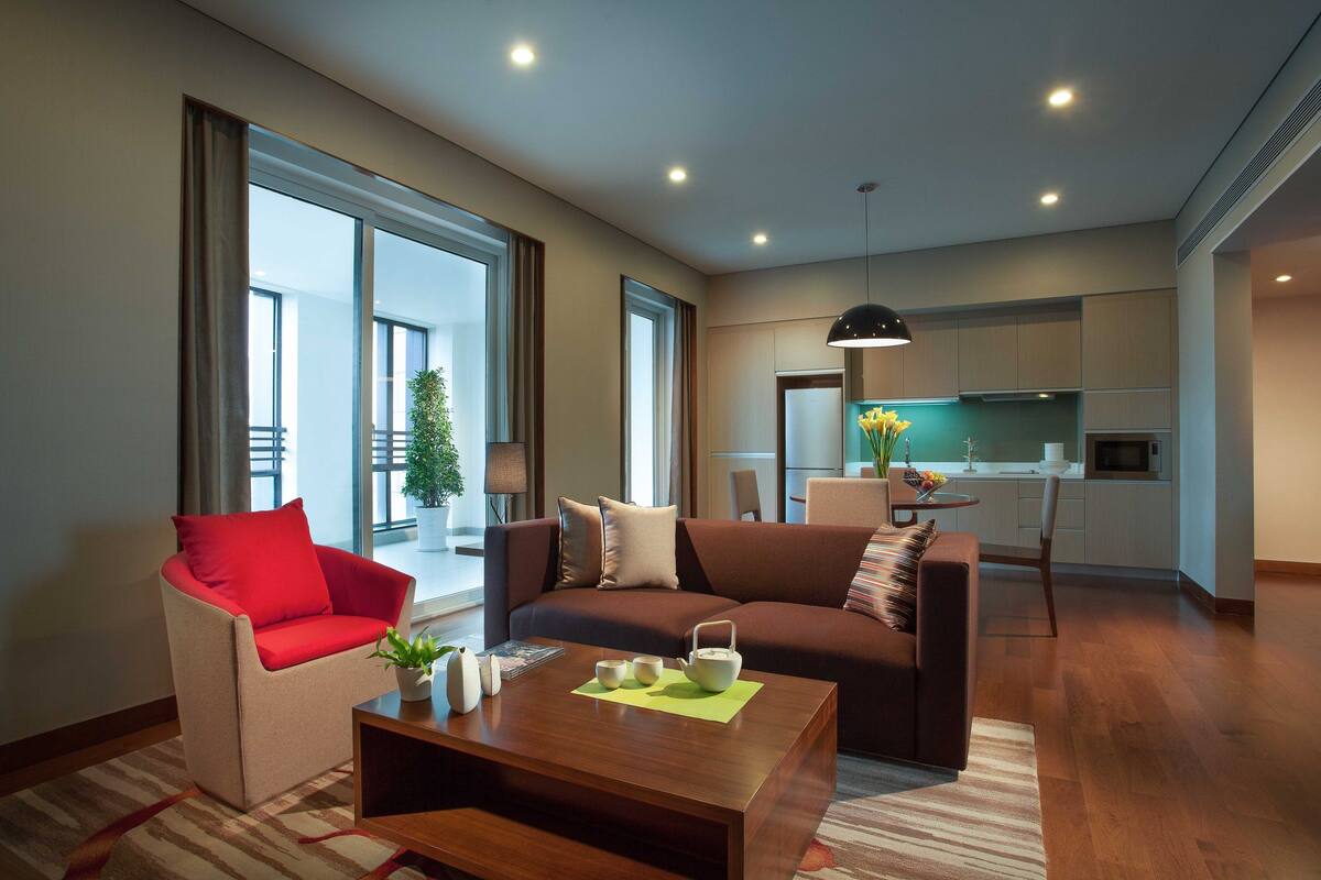 Un salon moderne comprenant un canapé, un fauteuil et une table basse, un coin cuisine et de grandes fenêtres offrant une vue dégagée.