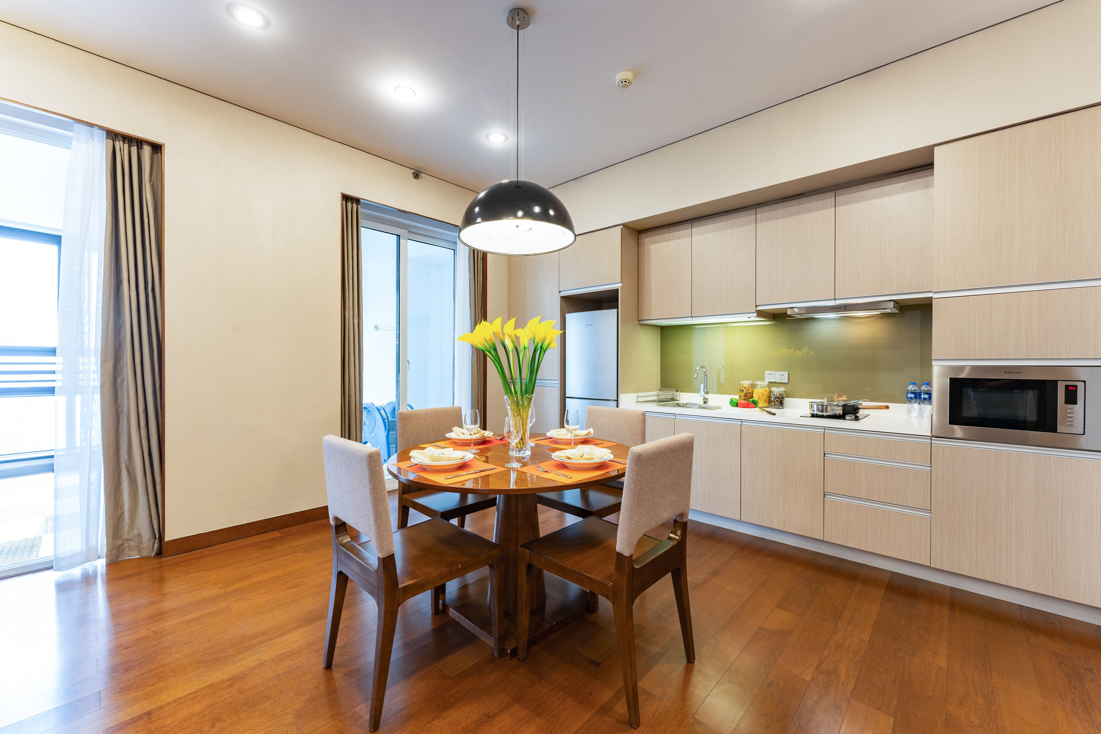 A modern kitchen with wooden cabinets, a dining table with chairs, and a pendant light.