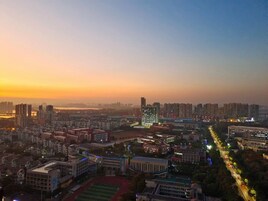 Paisagem urbana ao entardecer com edifícios altos, um campo esportivo e uma estrada bem iluminada.