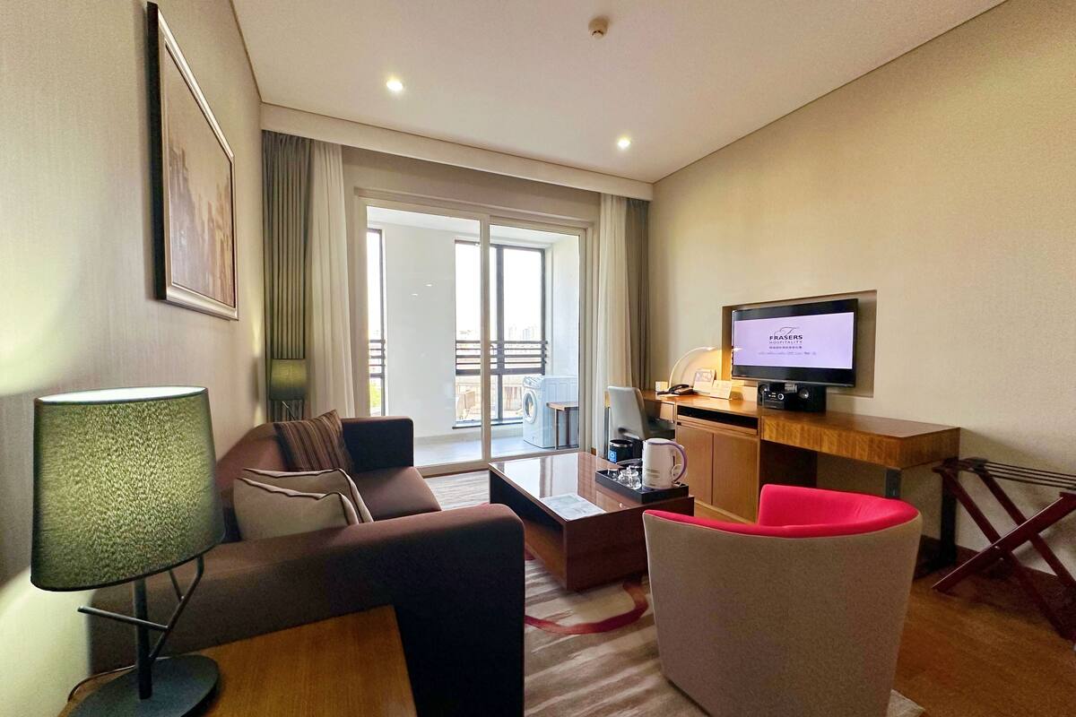 Une chambre d’hôtel moderne équipée d’un canapé, d’un fauteuil, d’une table basse et d’un téléviseur posé sur un bureau en bois.