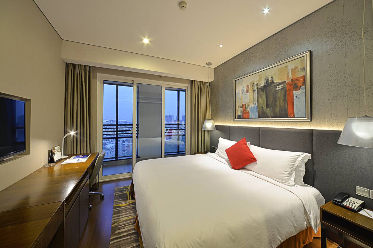 Une chambre d’hôtel avec un lit, un bureau, une télévision, un tableau et une vue sur la ville.