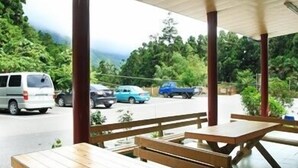 An outdoor covered area with wooden picnic tables and benches, surrounded by greenery and a view of parked cars. - Fenchihu Street Hotel (Zhuqi)