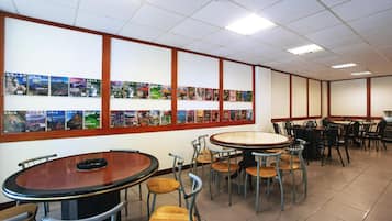 A dining area with round tables and chairs, a wall with framed pictures, and a tiled floor.