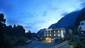 A hotel with a simple, rectangular structure, a parking lot, and a mountainous backdrop. - Fenchihu Street Hotel (Zhuqi)