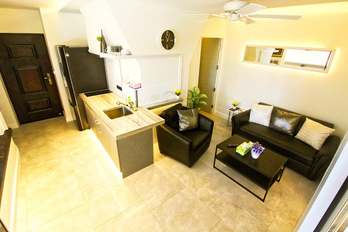 Un espacio habitable compacto con kitchenette, un sofá, una mesa de centro y un ventilador de techo.