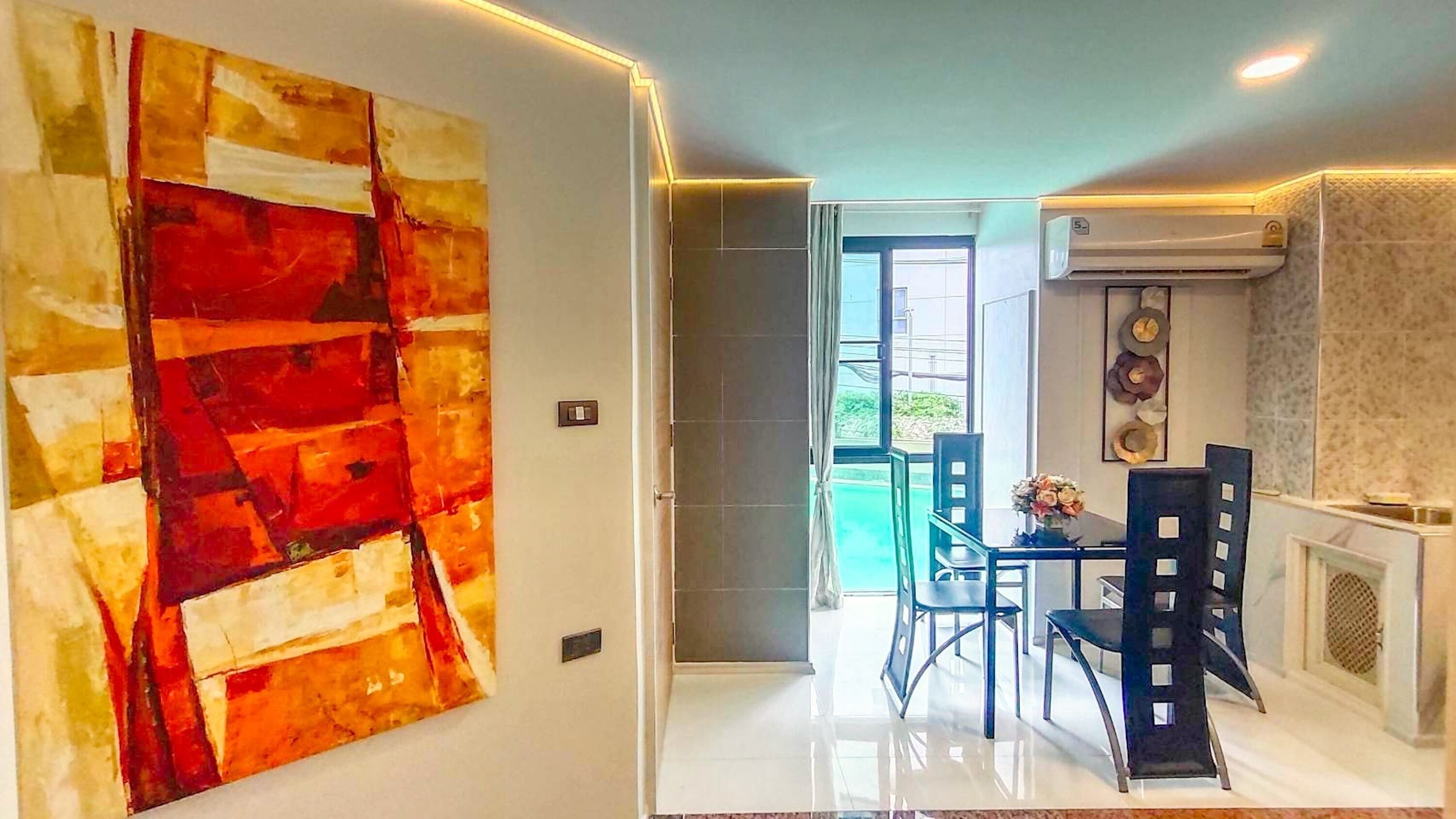 Uma área de jantar moderna com mesa e cadeiras de vidro, um quadro abstrato grande na parede e vista para o exterior.