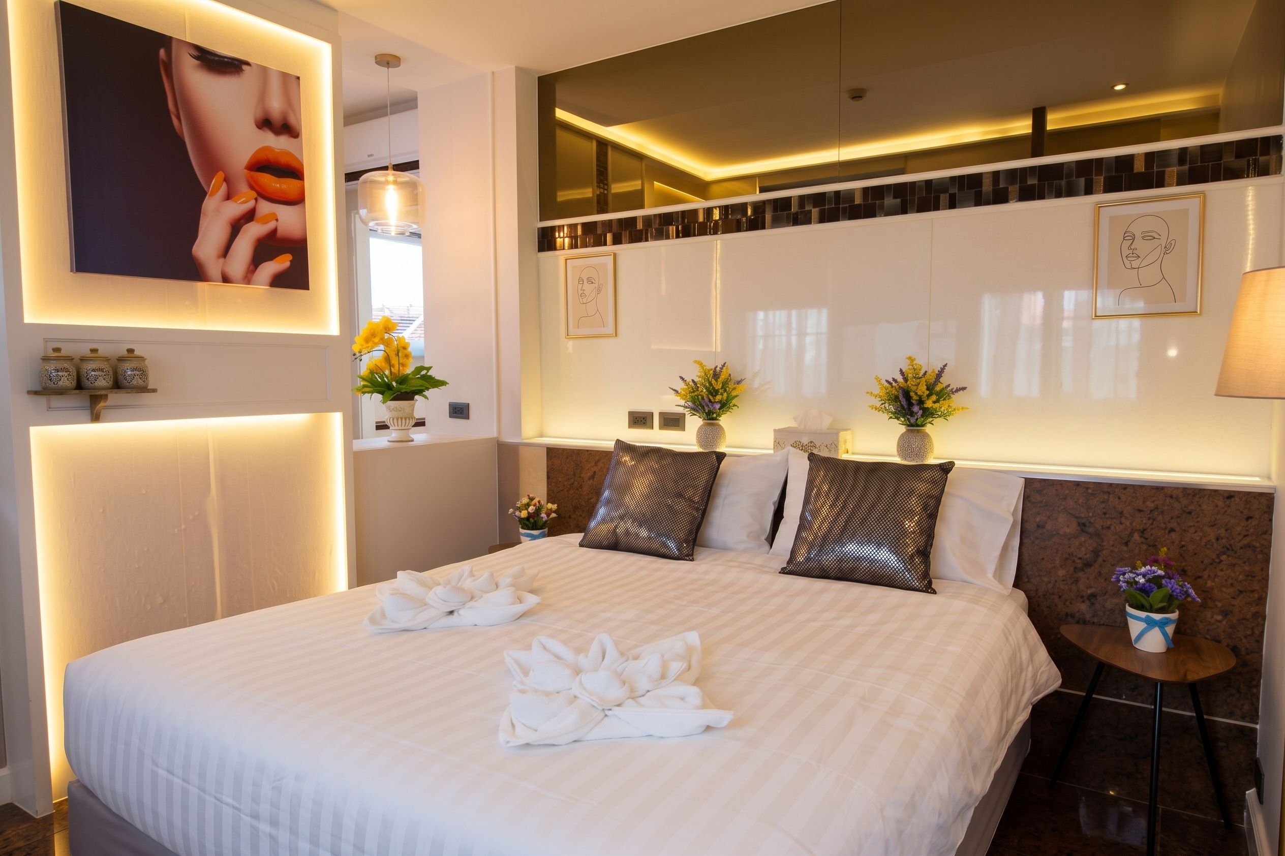 Une chambre d’hôtel avec un grand lit, une table de chevet avec une lampe, une petite table d’appoint avec un vase et des œuvres d’art accrochées aux murs.