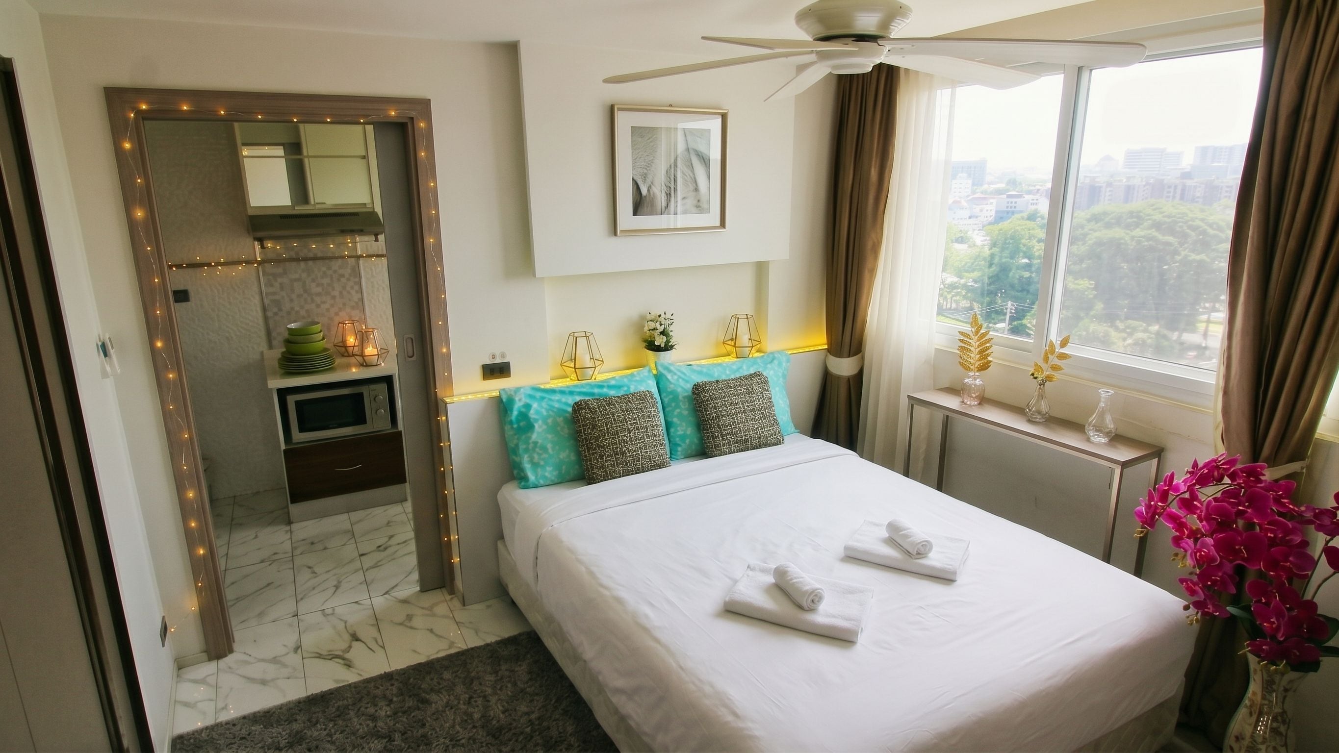 A hotel room with a bed, a desk, a window with a city view, and a bathroom with a mirror and lights.