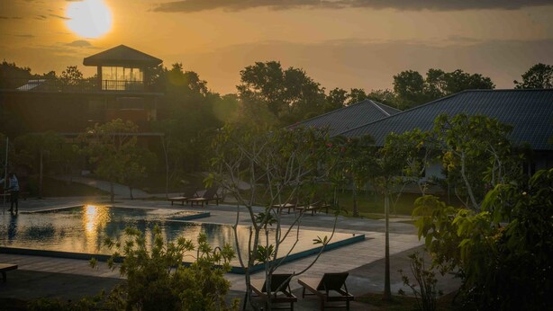 A serene pool area with lounge chairs, a gazebo, and a view of the sunset. - Sungreen Resort (Habarana)