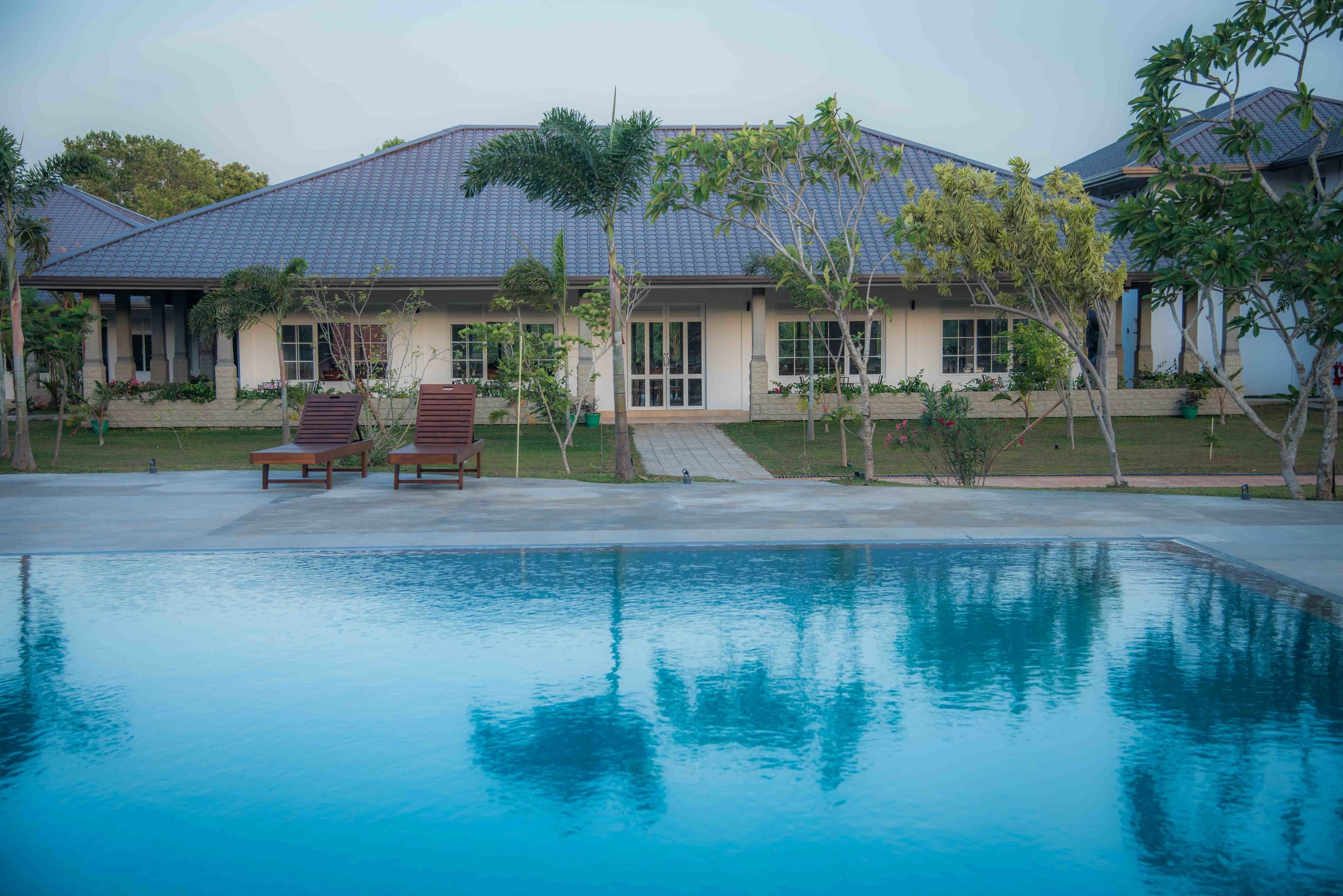 A house with a swimming pool, a covered patio, and a well-maintained lawn.