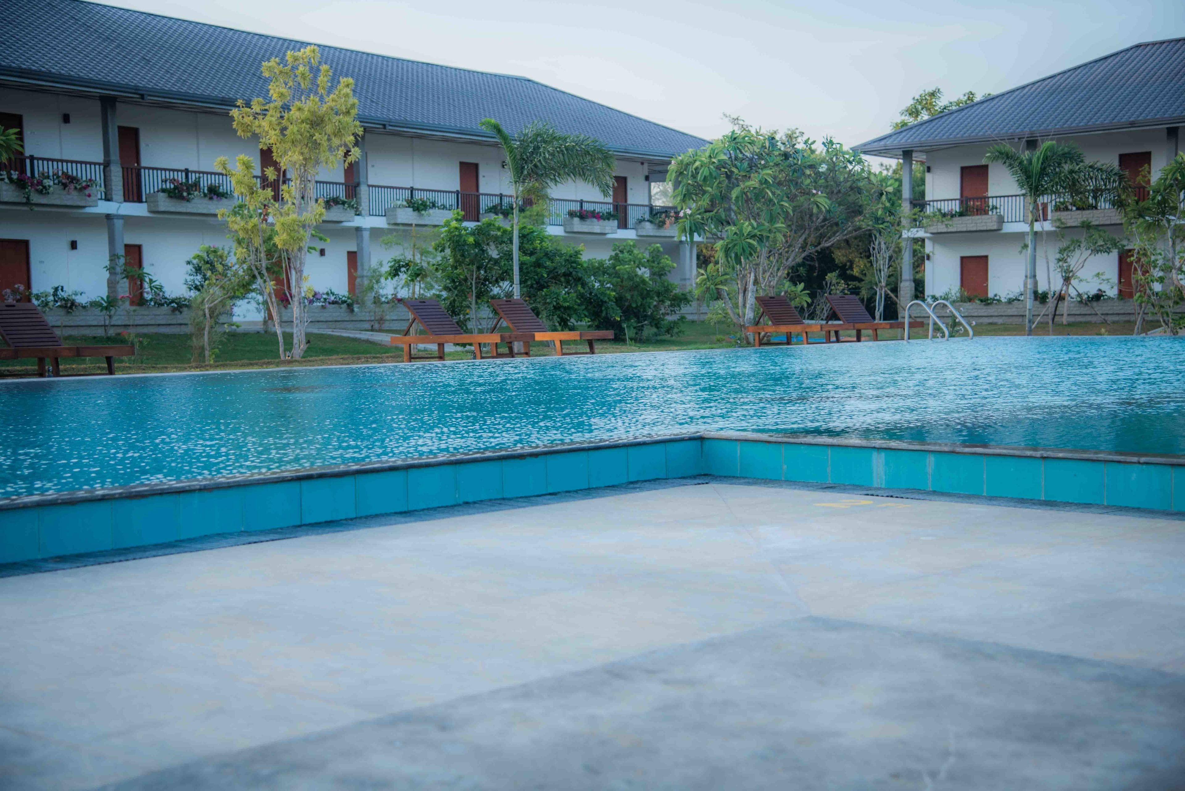 A swimming pool with lounge chairs and a building with balconies in the background.
