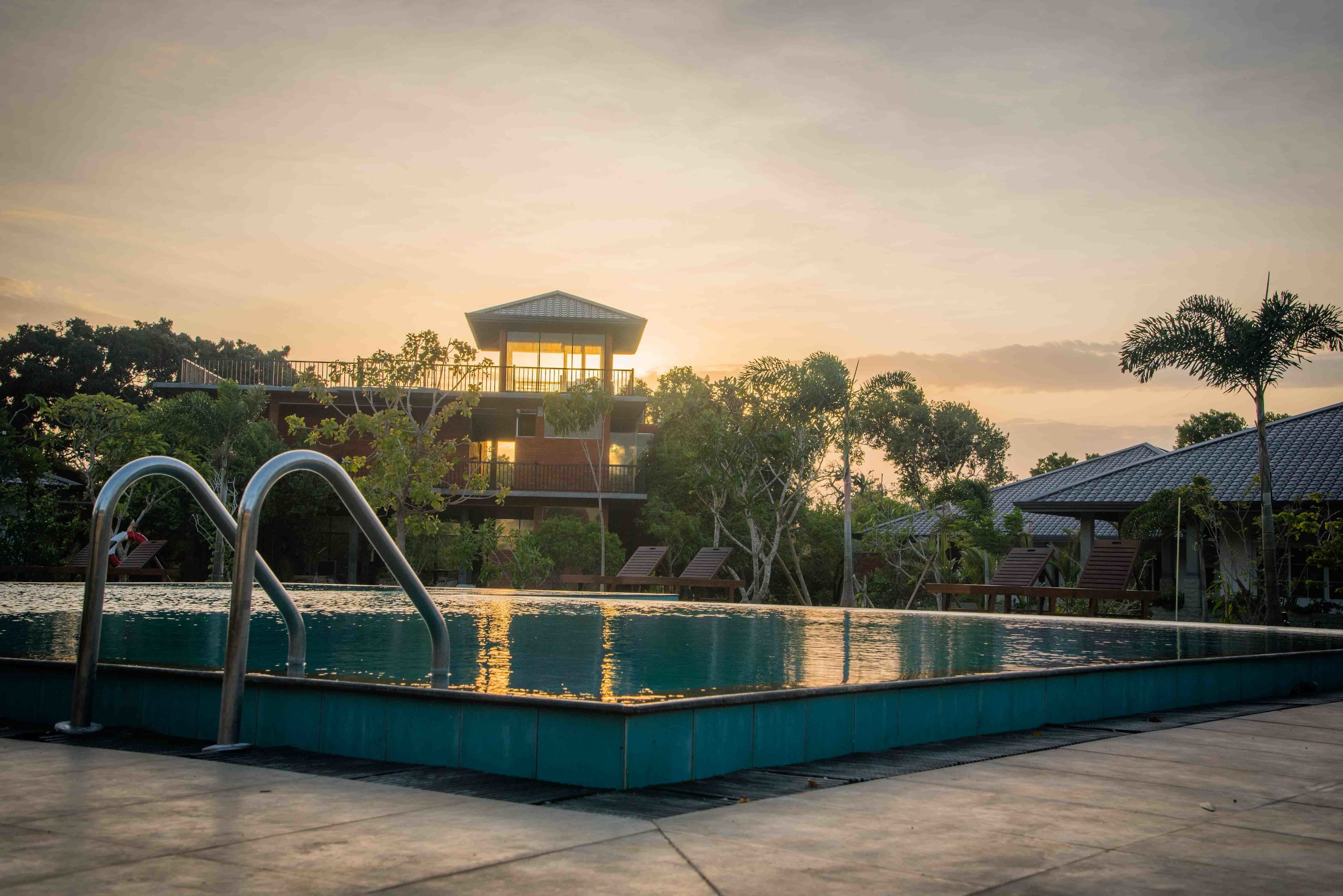 A swimming pool with metal railings, a building with a balcony, and trees in the background.